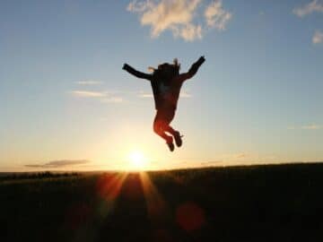 silhouette photo of a person jumping nearby green grass field during golden hour
